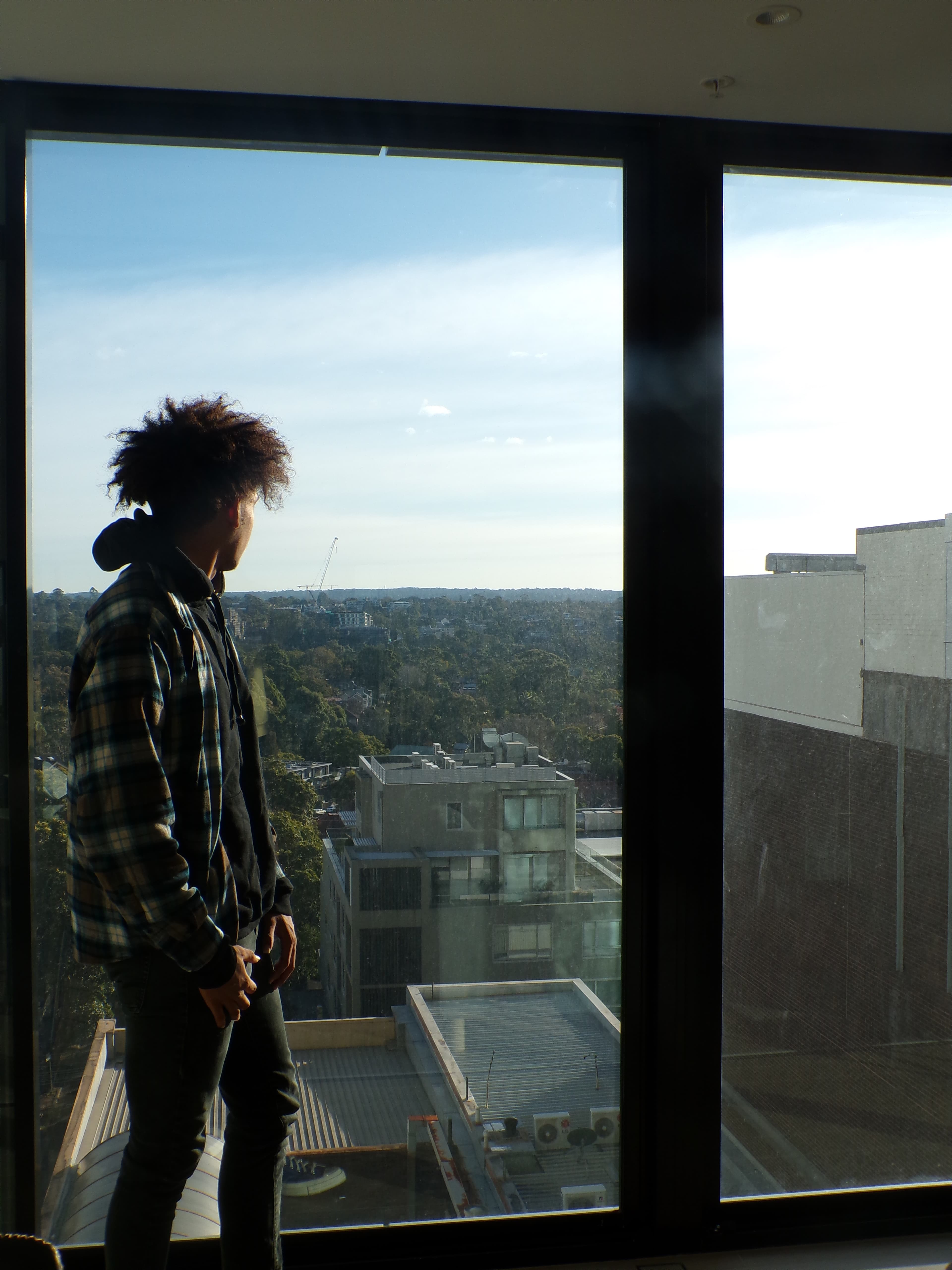 Joseph standing at a tall window, looking out over the trees and rooftops