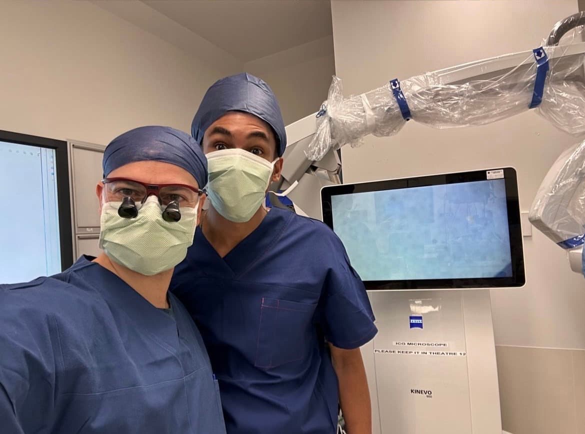 Joseph in surgical scrubs and a mask beside a colleague in an operating theatre